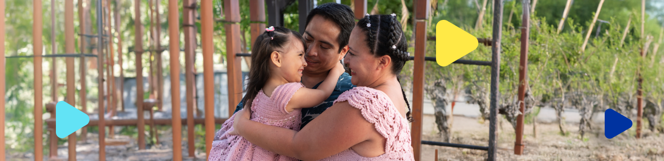Una famila de padre, madre y pequeña hija se abrazan en un parque.